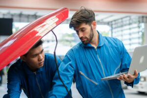 Car mechanic team using laptop boosting car engine at auto repair shop